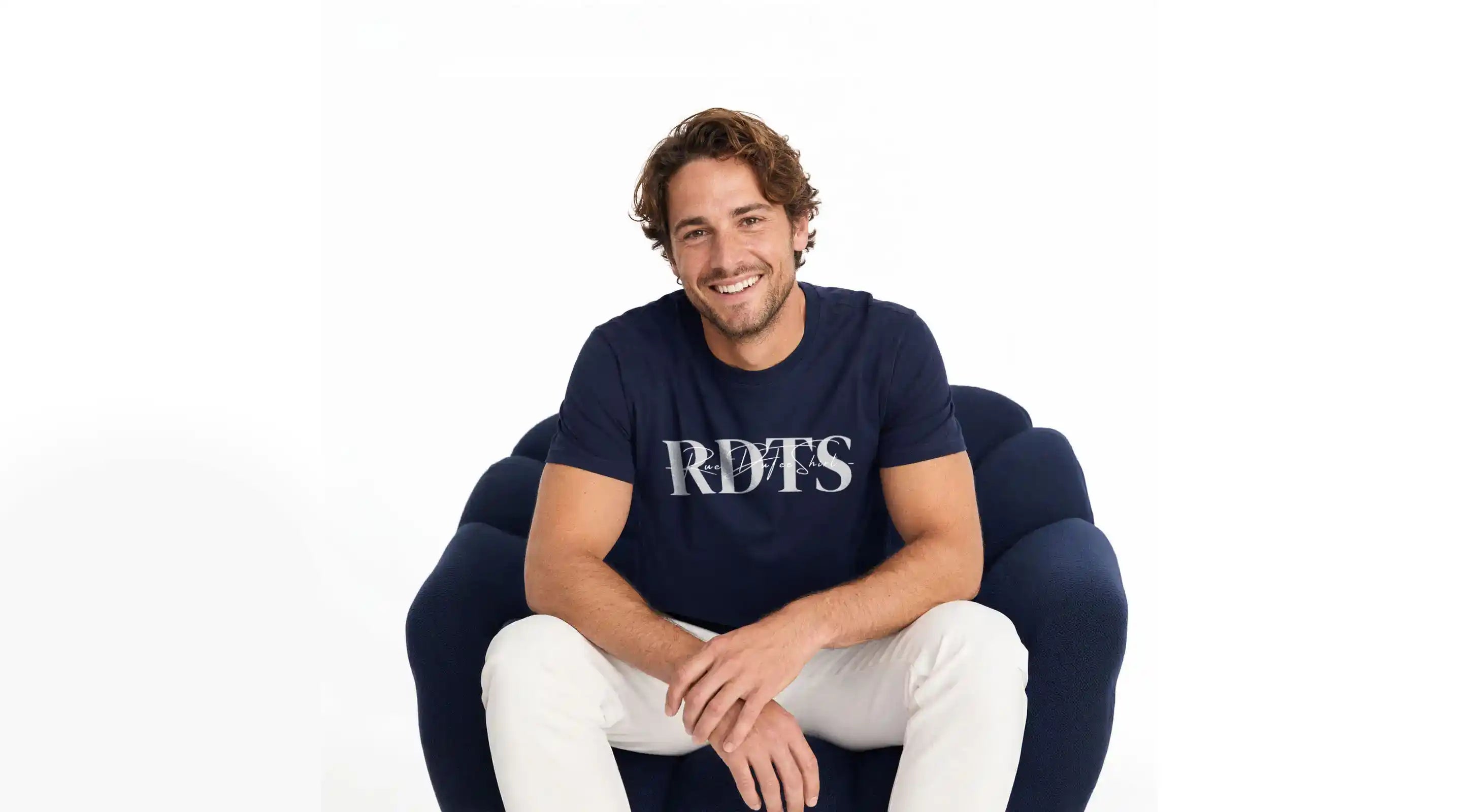 Bannière Rueduteeshirt - homme assis dans un fauteuil bleu marine portant un t-shirt bleu marine de qualité.